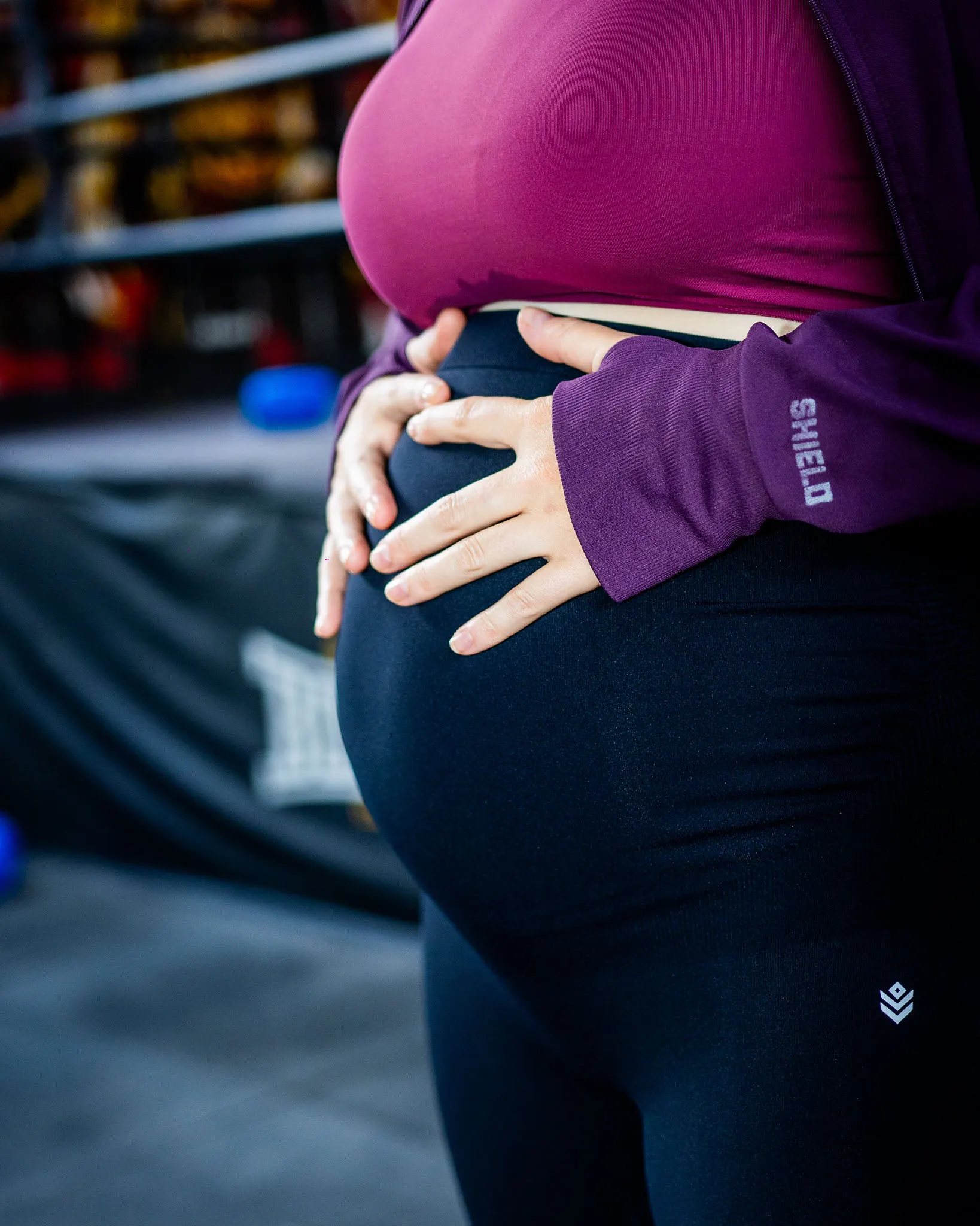 A pregnant woman with her hands on her bump, wearing Shield Mama Leggings
