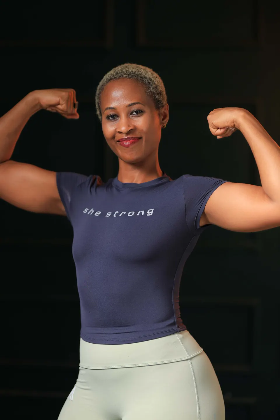 A woman flexing in the She Strong Community Tee in Navy